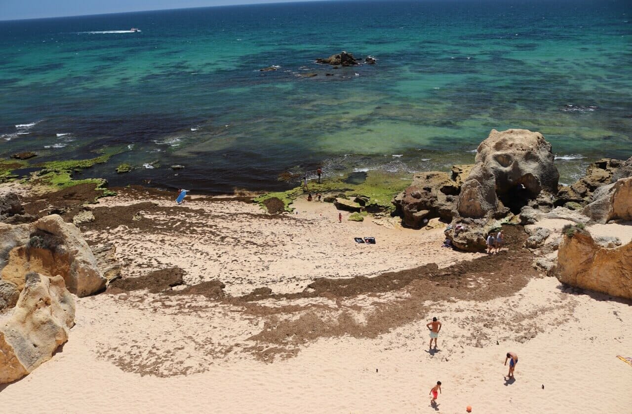 Três crianças jogando bola e o mar ao fundo na Praia da Vila Joya, Albufeira, Portugal