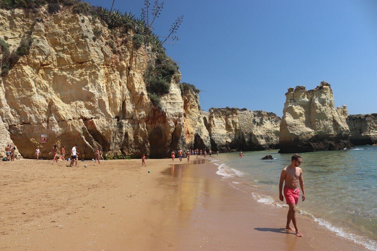 los enormes acantilados amarillos de Praia do Pinhão, en Lagos, y un hombre con pantalones cortos rosa caminando por la playa