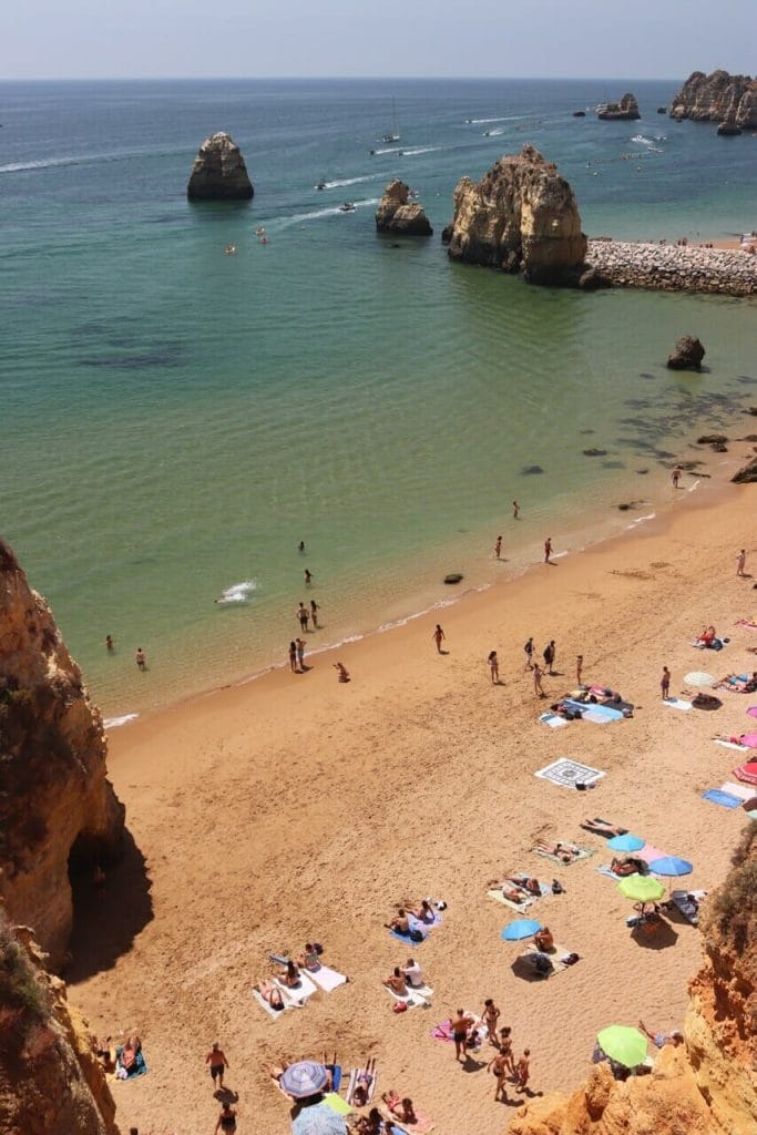 vista aérea da Praia do Pinhão, com guarda-sóis de diferentes cores, toalhas na areia, gente tomando sol e em pé, águas cristalinas e falésias