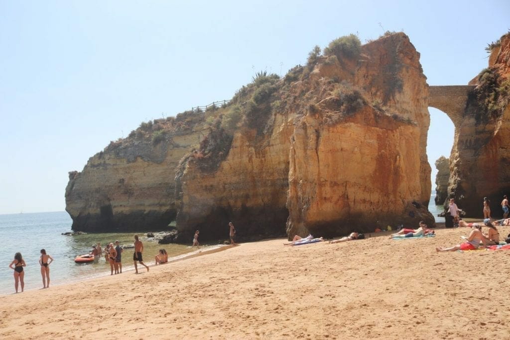 part of Praia dos Estudantes with some yellow cliffs, people waling on the shore and sunbathing