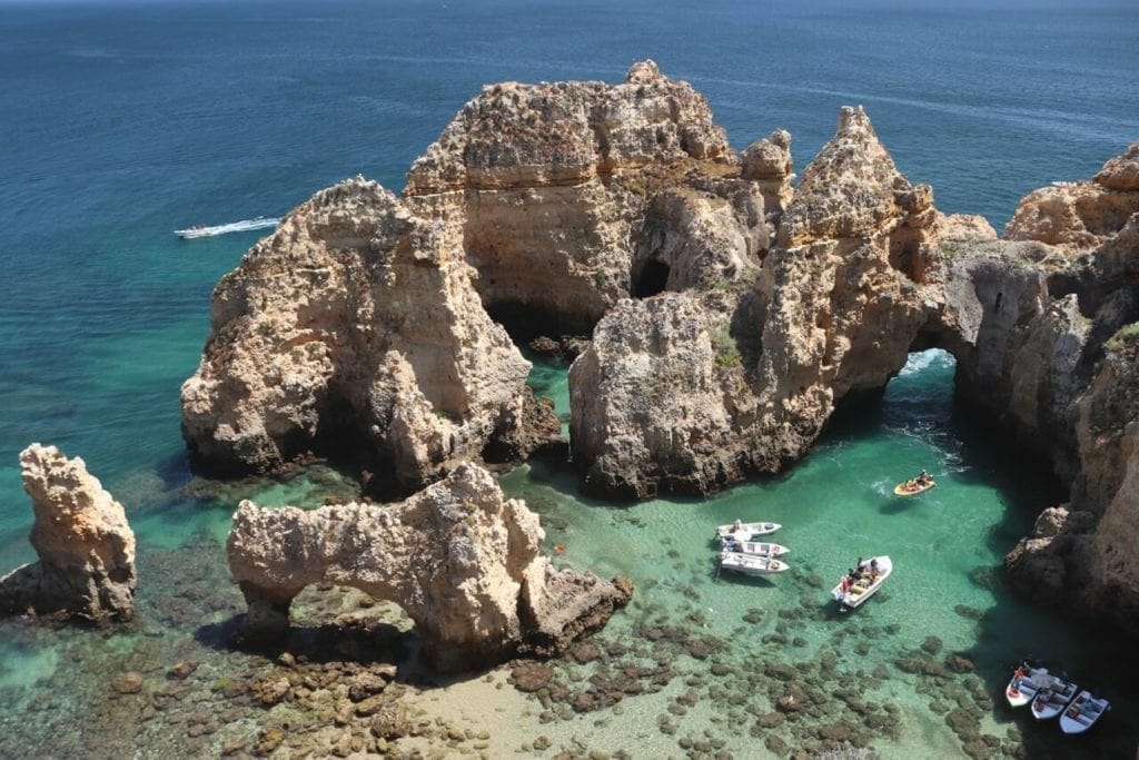 The crystal-clear emerald water of Ponta da Piedade, in Lagos, with some boats sailing and yellow limestone cliffs with splendid rock formations and sea arches.