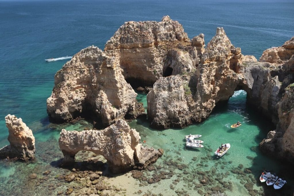 As águas cristalinas da Ponta da Piedade, em Lagos, com alguns barcos e falésias calcárias amarelas com esplêndidas formações rochosas e arcos marítimos