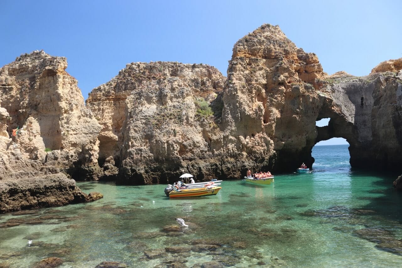 Four boats sailing on the unbelievable crystal-clear green water of Ponta da Piedade surrounded by uneven beige cliffs 