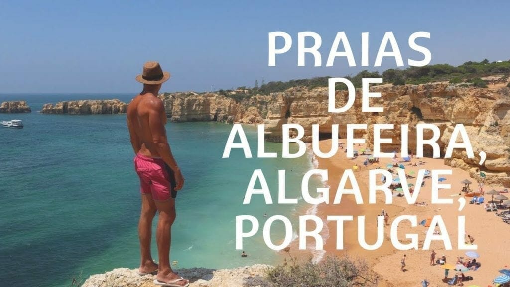 Um homem com um chapéu castanho e uma short vermelho de pé no topo de uma falésia na Praia da Coelha, Albufeira, Portugal
