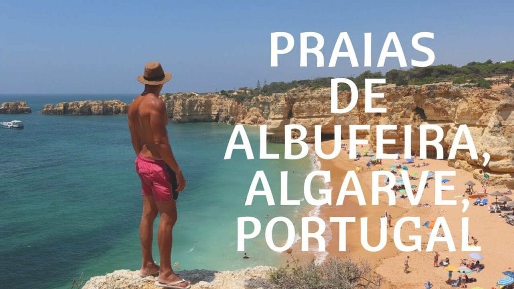 Un hombre vestido con un sombrero marrón y un short rojo de pie en la cima de un acantilado en Praia da Coelha, Albufeira, Portugal