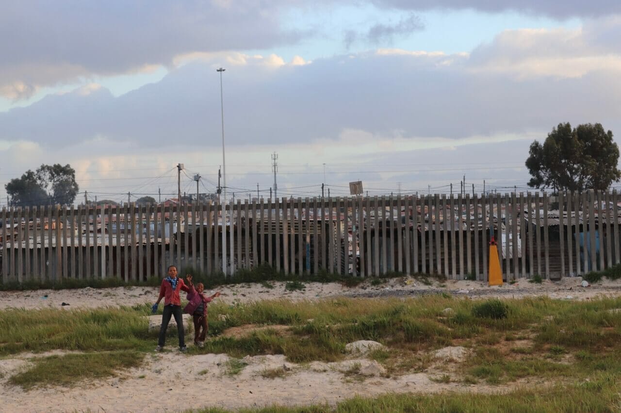 Two kids playing in front near the roads and a township behind them, in the suburbs of Cape Town, South Africa