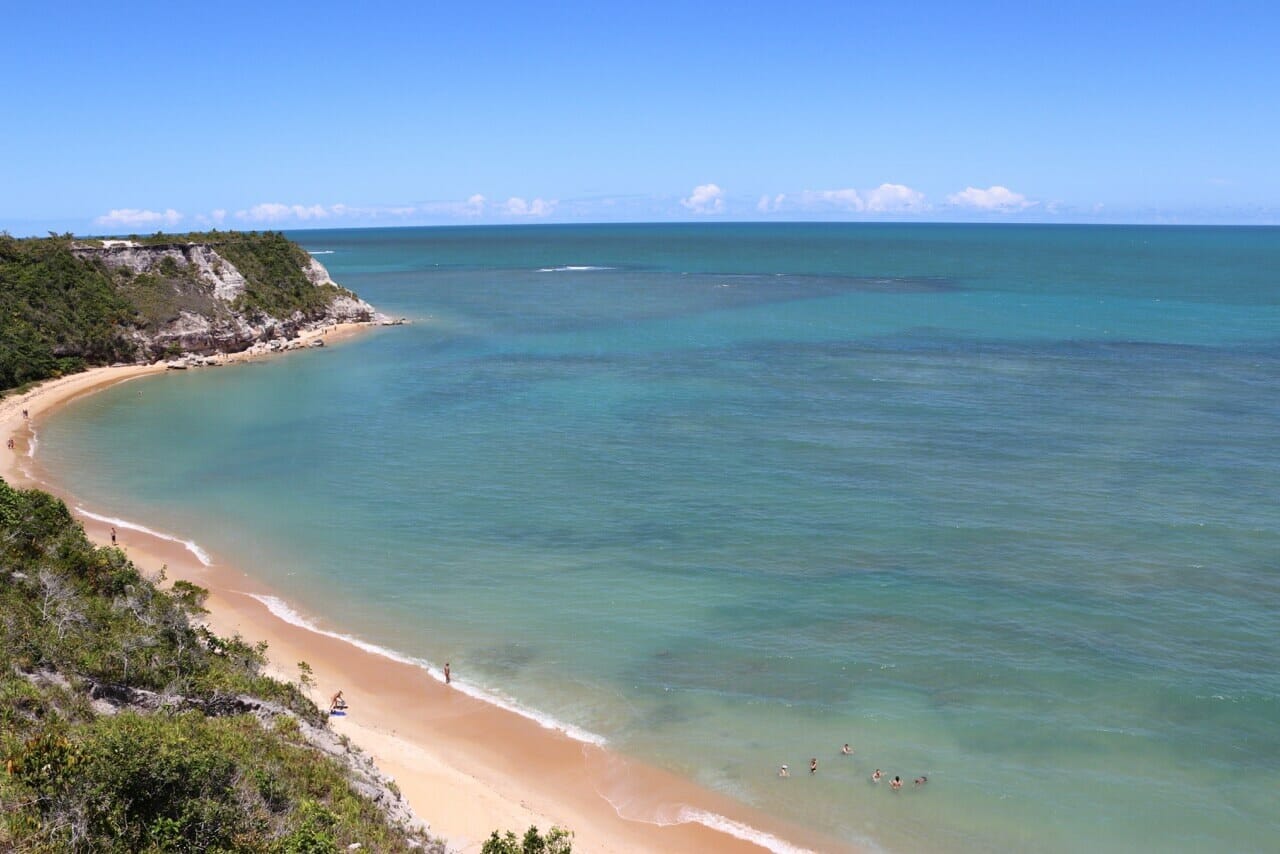 As águas azuis cristalinas cercada por falésias cobertas com vegetação na Praia do Espelho, Porto Seguro, Bahia