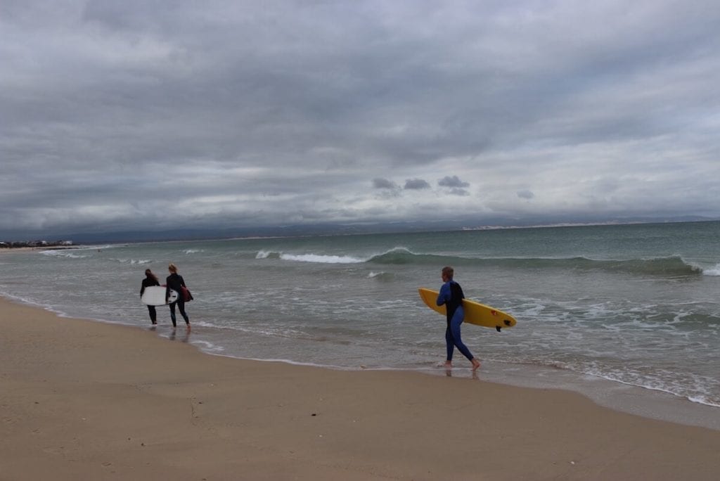 três surfistas andando na praia em Jeffreys Bay, África do Sul