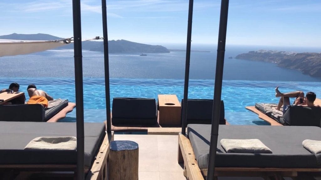 people lying on lounge chairs by the infinity pool of the hotel Cavo Tagoo Santorini 