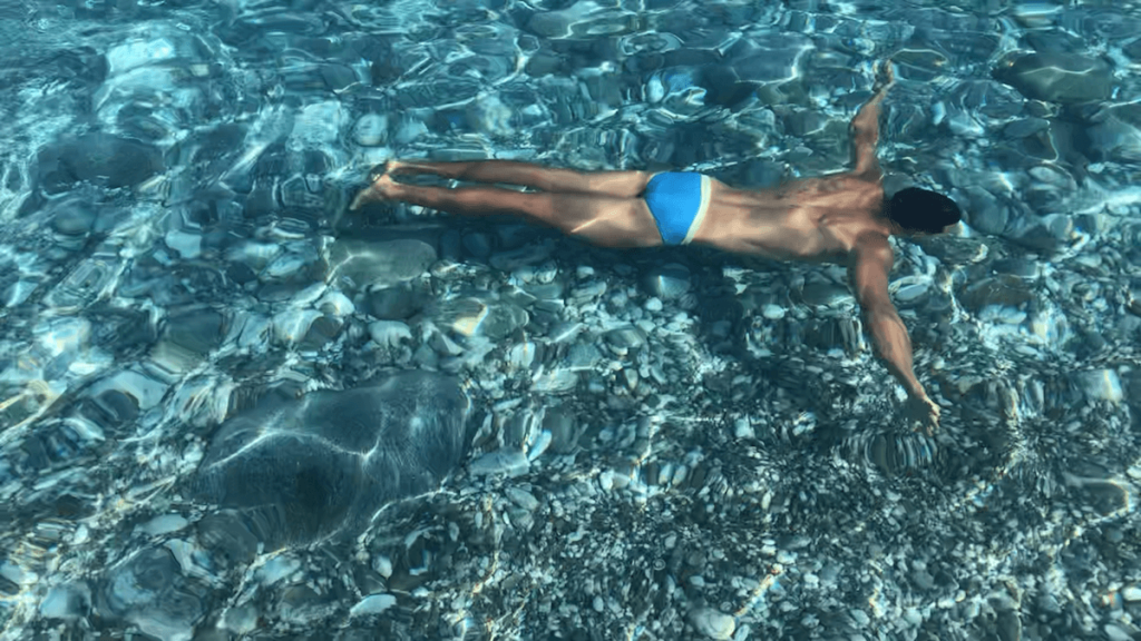 A man swimming in the crystal-clear waters of Katergo Beach, Folegandros, Greece