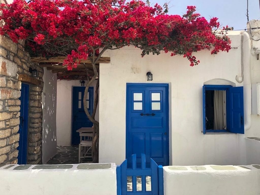 A white-washed house with blue windows and doors with red bougainvillea on the top of it, Folegandros, Greece