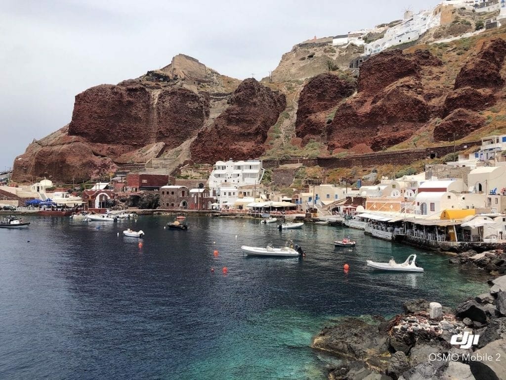 barcos na água e casas caiadas de branco cercadas por falésias vermelhas  de calcário colossais na Baía de Ammoudi, Santorini, Grécia
