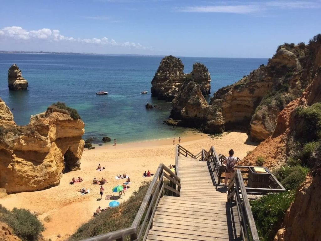 Uma escadaria de madeira que dá acesso à Praia do Camilo, em Lagos, que é rodeada por falésias vermelho-amareladas e tem águas azuis calmas