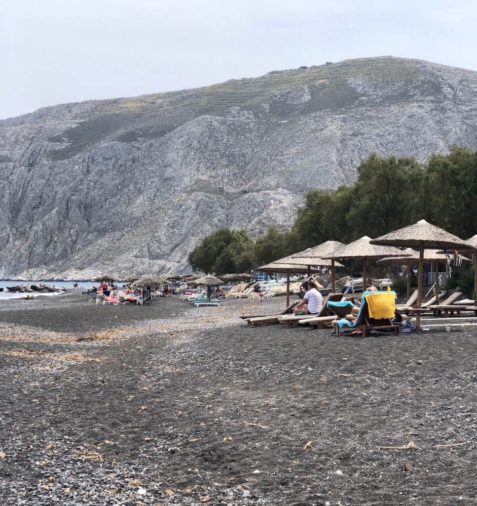 Alguns guarda-sóis, espreguiçadeiras na praia de Kamari, Santorini e a Montanha Mesa Vuono ao fundo