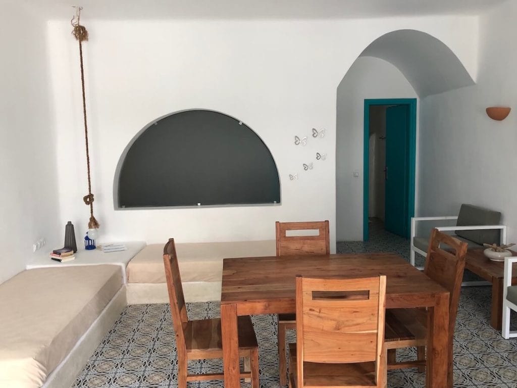 Un apartamento de Nissia Beach Apartments & Suites en Kamari, Santorini, con paredes blancas, sofás beige y una mesa de madera con sillas