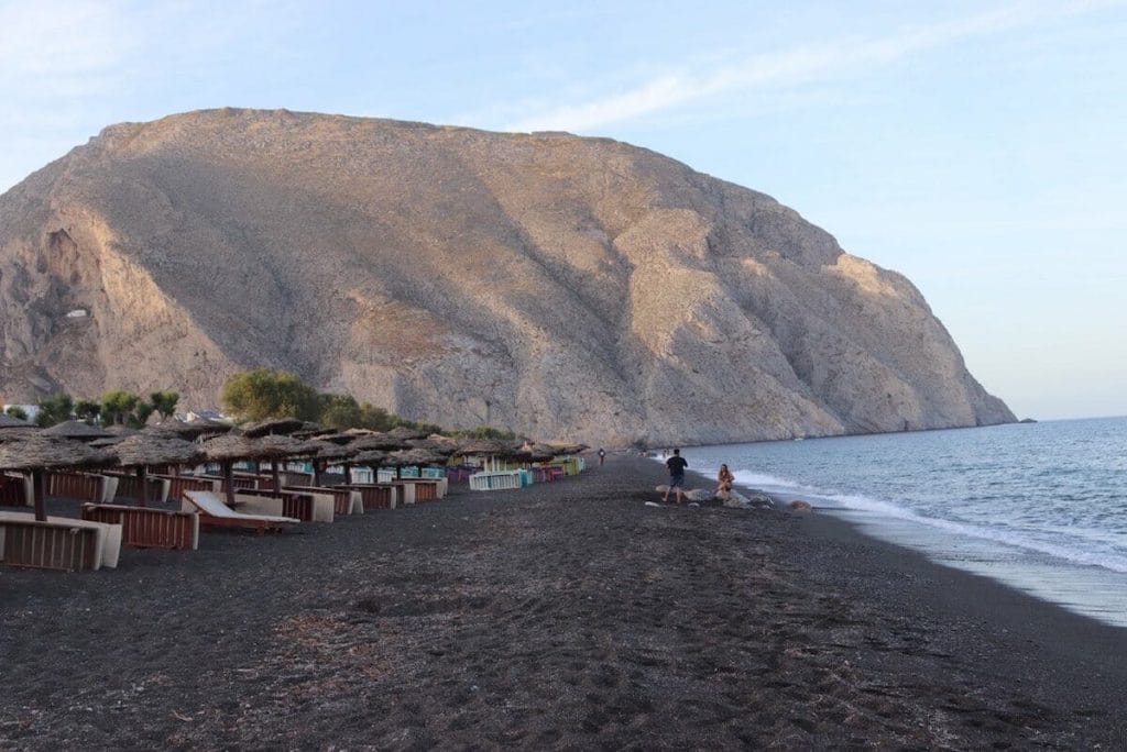 Perissa Black Sand Beach, Santorini, with some lounge chairs, umbrellas and the Mesa Vuono Mountain in the background