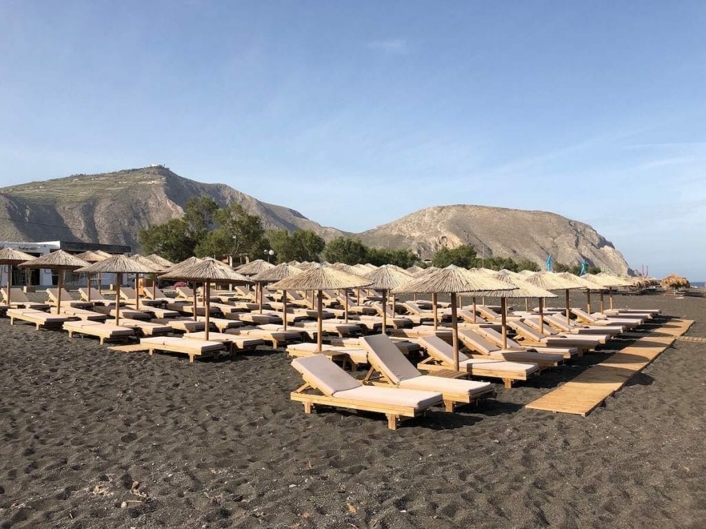 lounge chairs and umbrellas on the Perissa Beach, Santorini, and Mesa Vuono Mountain in the background