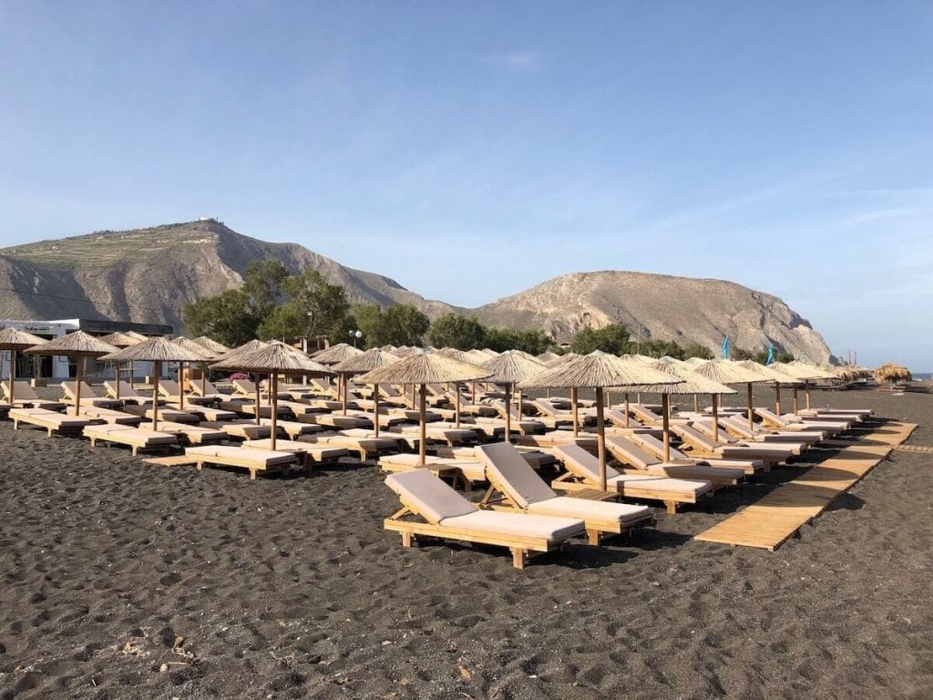 lounge chairs and umbrellas on the Perissa Beach, Santorini, and Mesa Vuono Mountain in the background