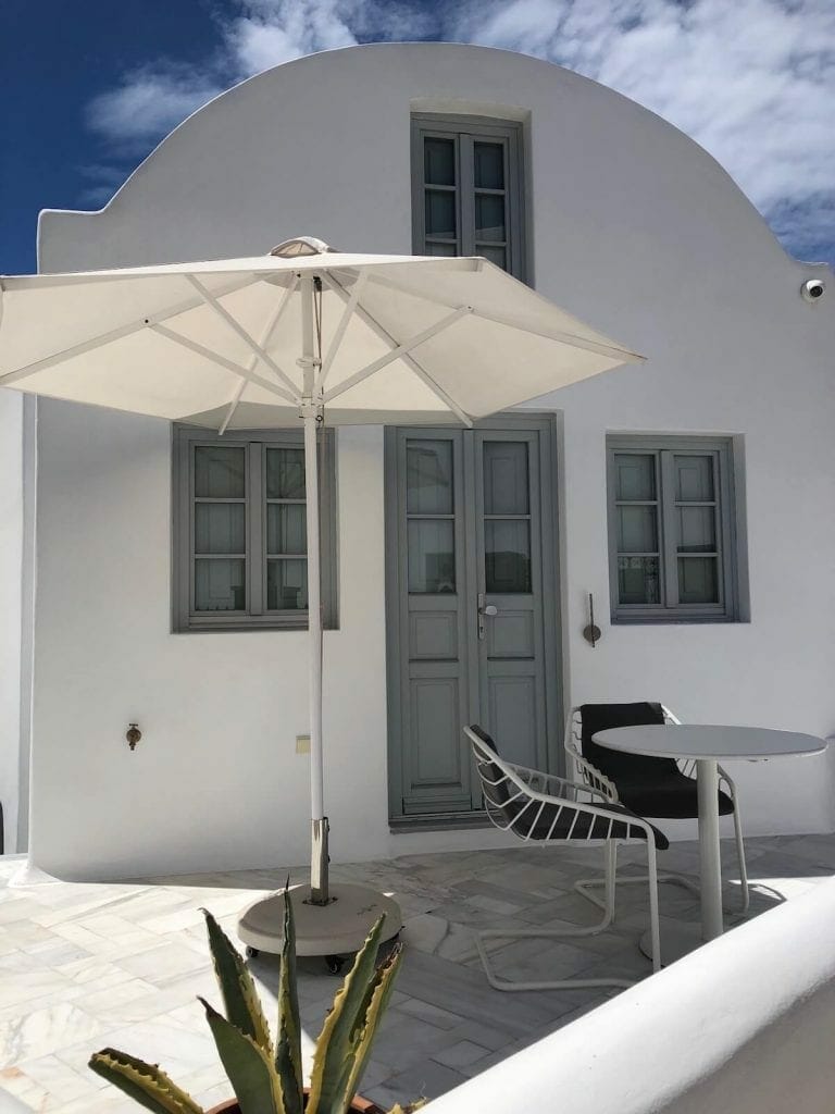 Uma villa caiada de branco com guarda-sol, mesa e cadeiras no terraço em Imerovigli, Santorini