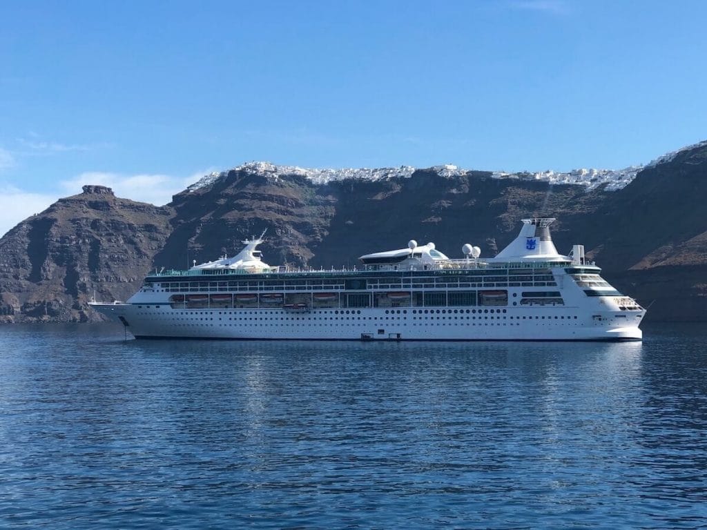 A cruise ship in Santorini and cliffs with white-washed houses villages on the top of it