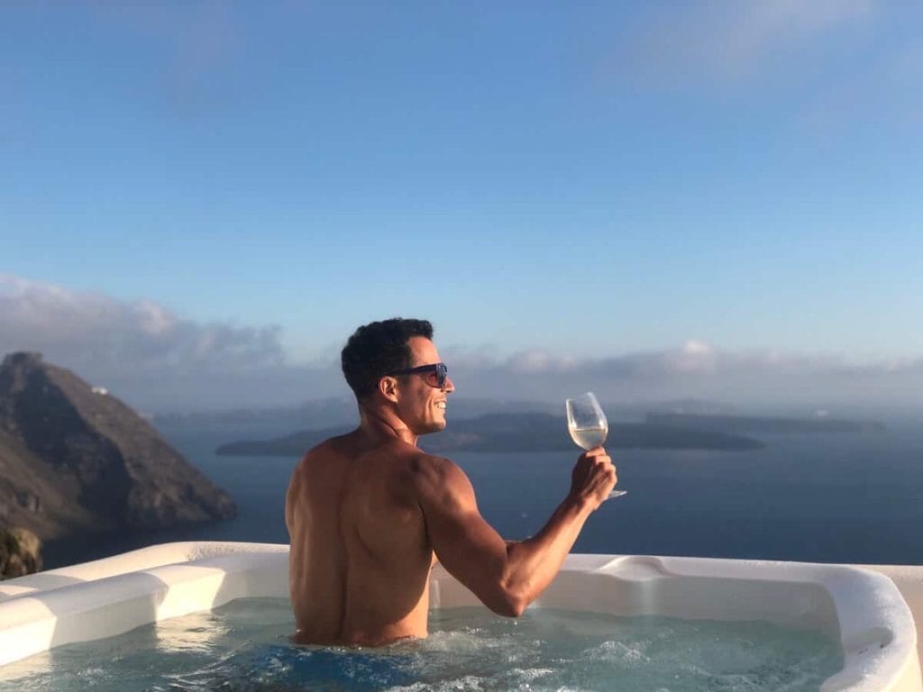 Pericles Rosa in a jacuzzi having a glass of white wine in a luxury hotel in Santorini, Greece