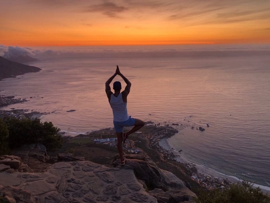 A man on an yoga tree pose during the sunset at top of Lion's Head, Cape Town