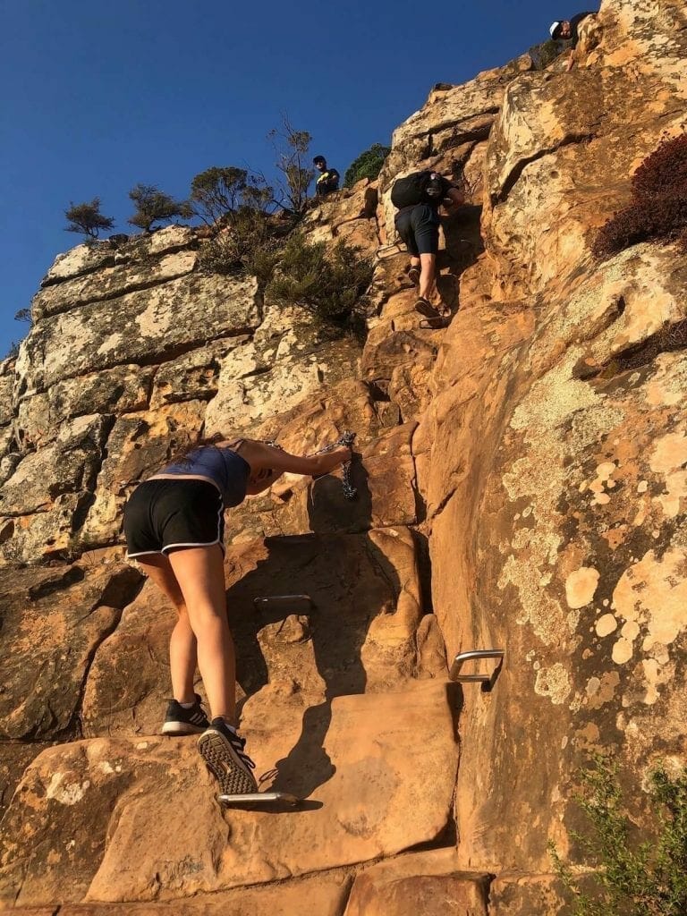 a young lady and a man climbing up the staples to the top of Lion's Head