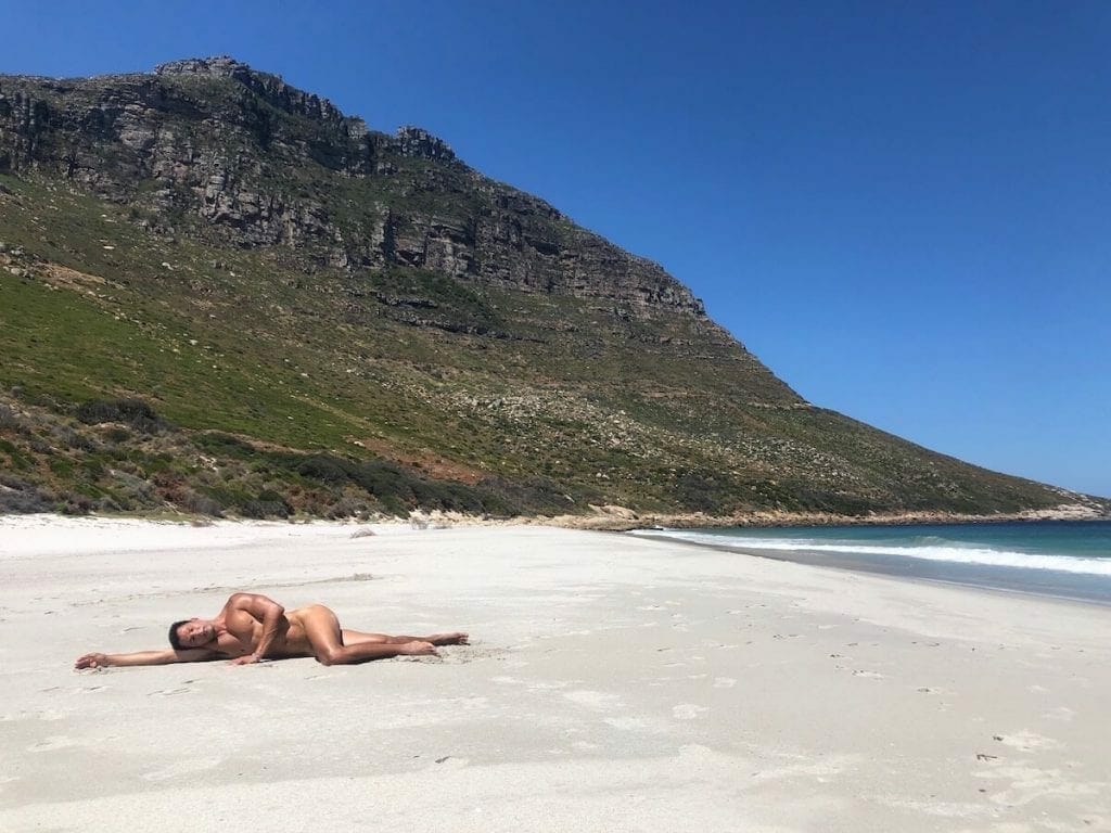un hombre tombado en la arena a tomar sol desnudo en Sandy Bay Beach, Ciudad del Cabo, Sudáfrica