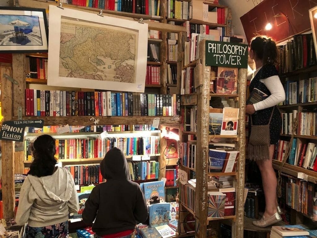 Three people among books on the shelves at Atlantis Bookshop, Oia, Santorini
