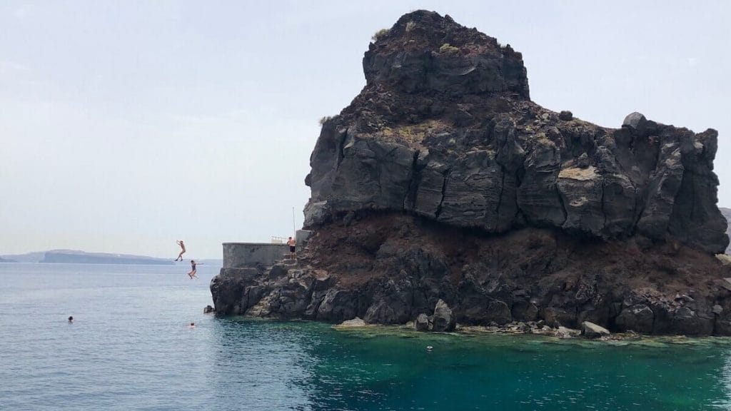 Duas mulheres pulando de um penhasco na Baía de Ammoudi, em Santorini