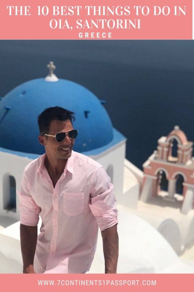 a man wearing sunglasses and a pink shirt and a blue-domed church with a salmon bell tower and the Aegean Sea in the background, in the town of Oia, Santorini