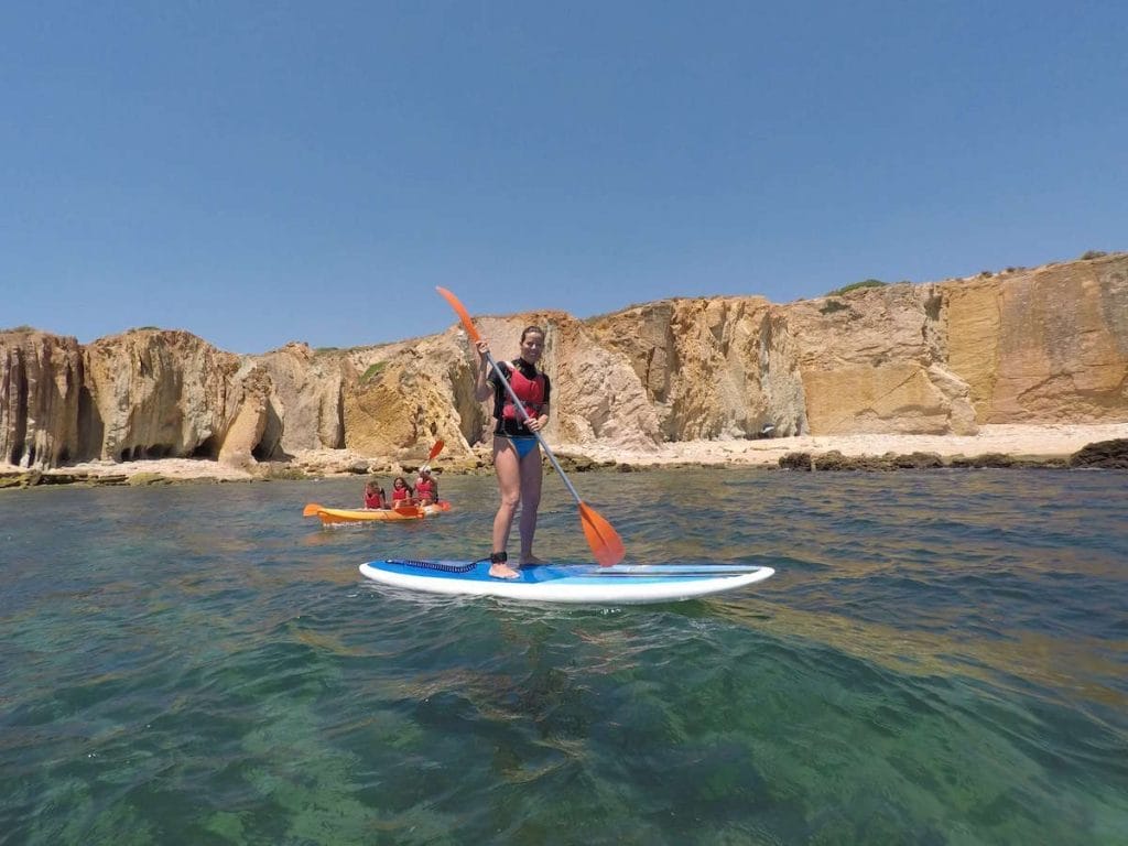 Uma mulher fazendo SUP en duas crianças e um adulto em um caiaque na Praia dos Arrifes, Albufeira