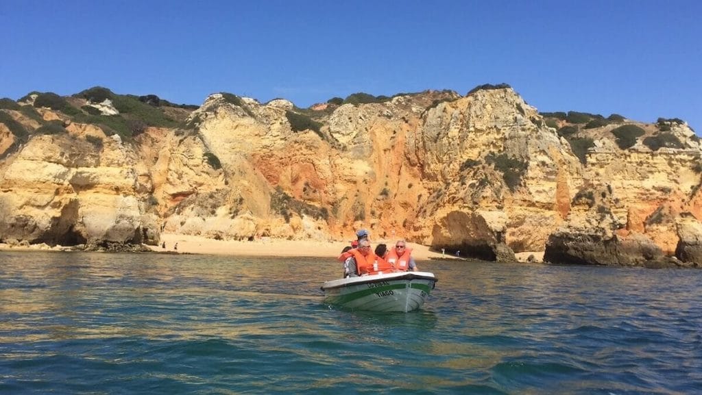 three people wearing red lifejackets on a boat trip to Ponta da Piedade with some massive limestone cliffs behind them