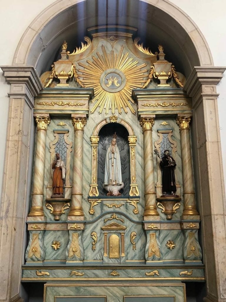 Un arco de altar de mármol con algunos detalles dorados y tres pequeñas estatuas de santos, en la Iglesia de Nossa Senhora da Conceição en Albufeira