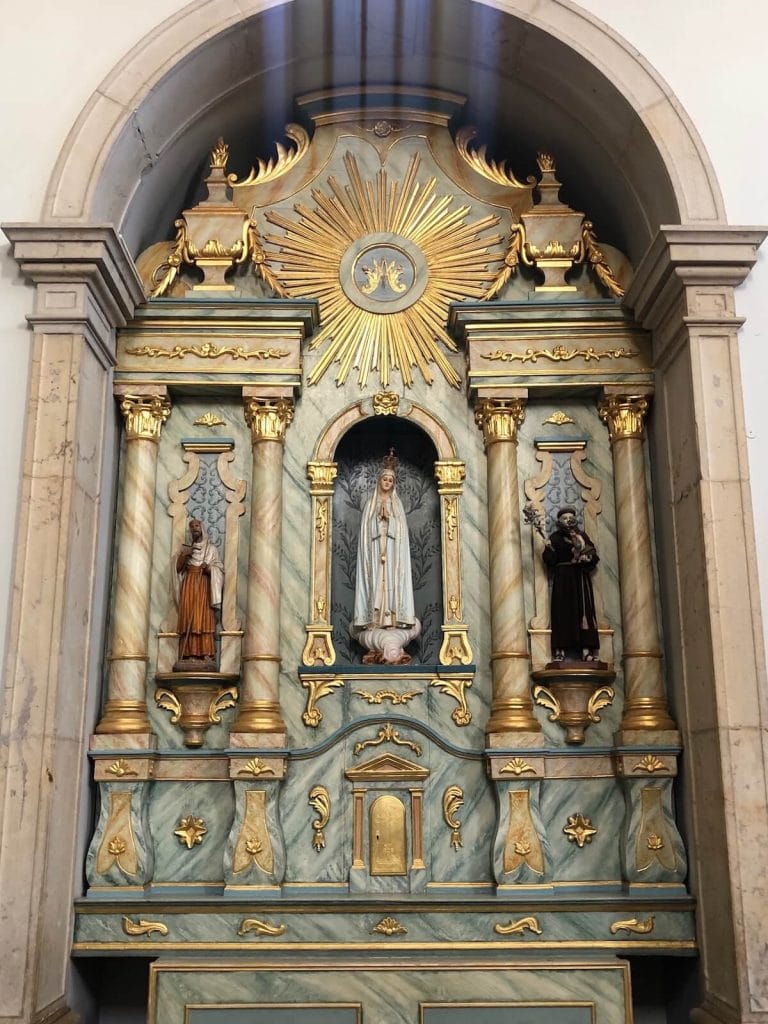 Um altar em arco de mármore com alguns detalhes dourados e três pequenas estátuas de santos, na Igreja de Nossa Senhora da Conceição em Albufeira