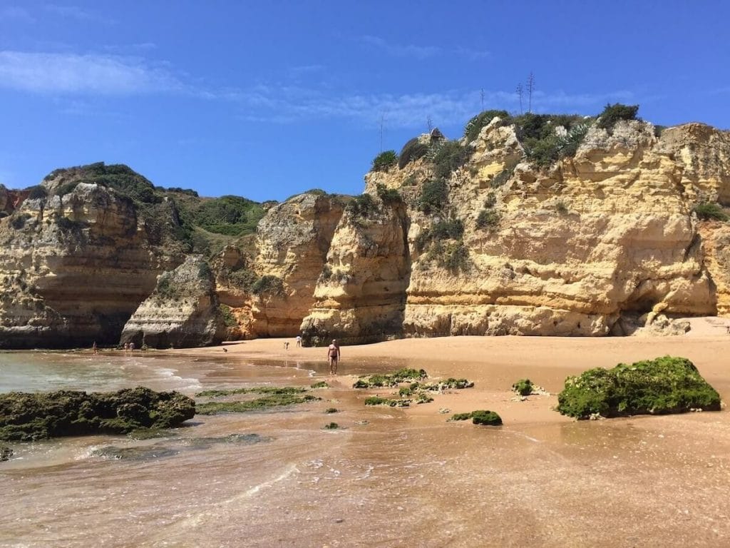 Um homem caminhando entre as falésias da Praia de Dona Ana, Lagos, Portugal