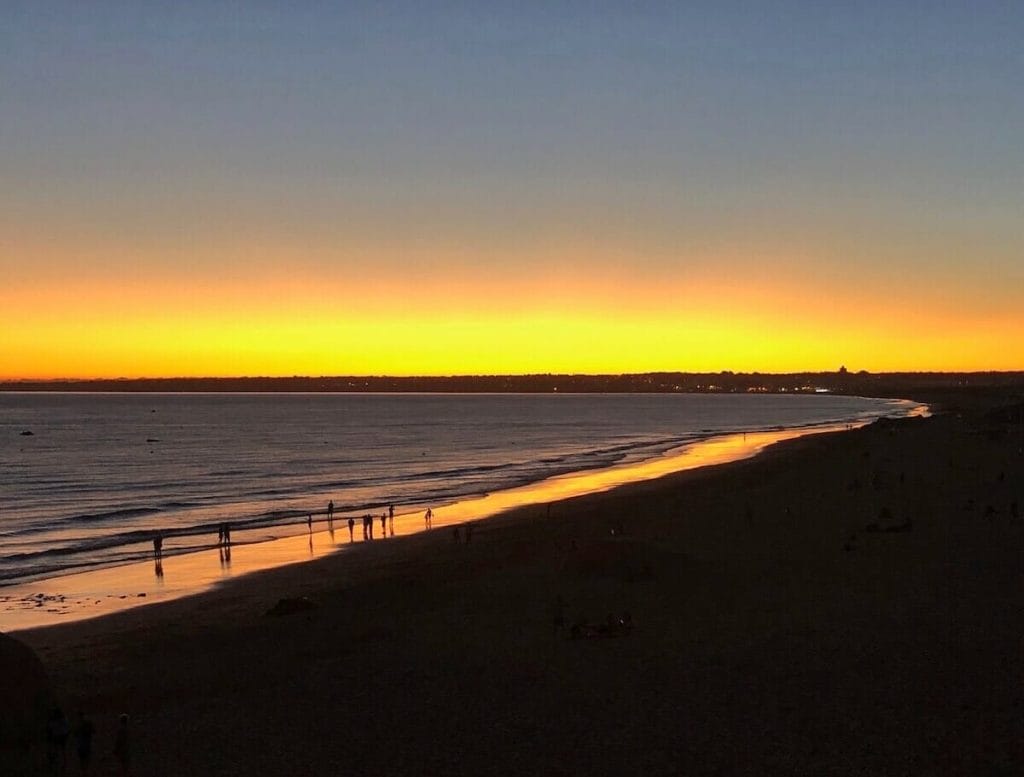 Praia da Galé, Albufeira, depois do pôr do sol com o céu e parte da areia coloridos com tons dourados vibrantes