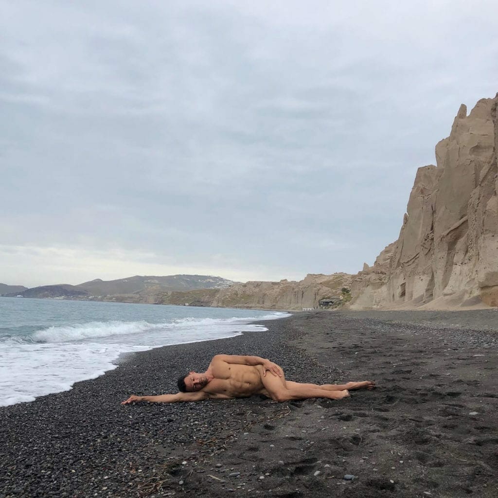 A man laying down on the black sand of Vlichada Beach, Santorini
