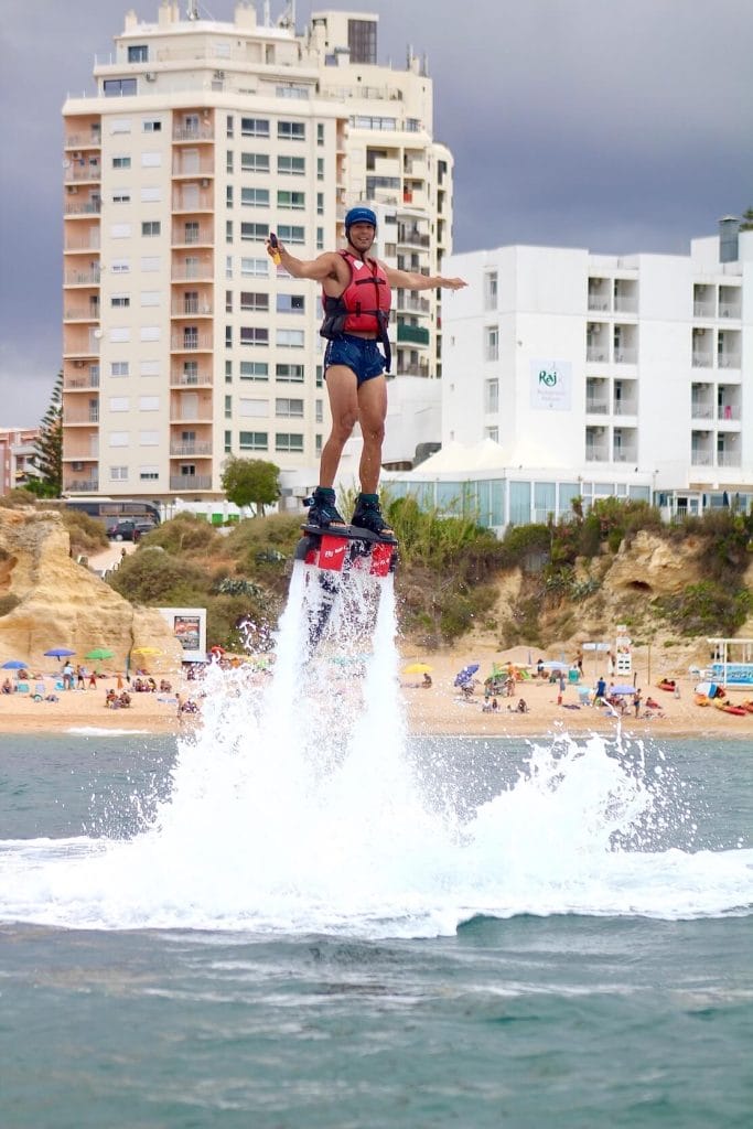 Pericles Rosa vestindo um short azul, colete salva-vidas vermelho e capacete azul a voar sobre a costa algarvia num flyboard na Praia de Armacão de Pêra