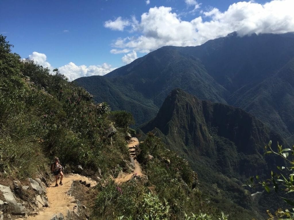Una mujer subiendo el sendero a la montaña Machu Picchu con varias montañas al fondo, Perú