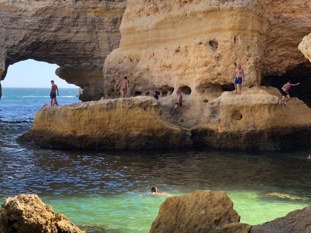 Algunas personas caminando y saltando desde los acantilados en el agua en Praia da Marinha