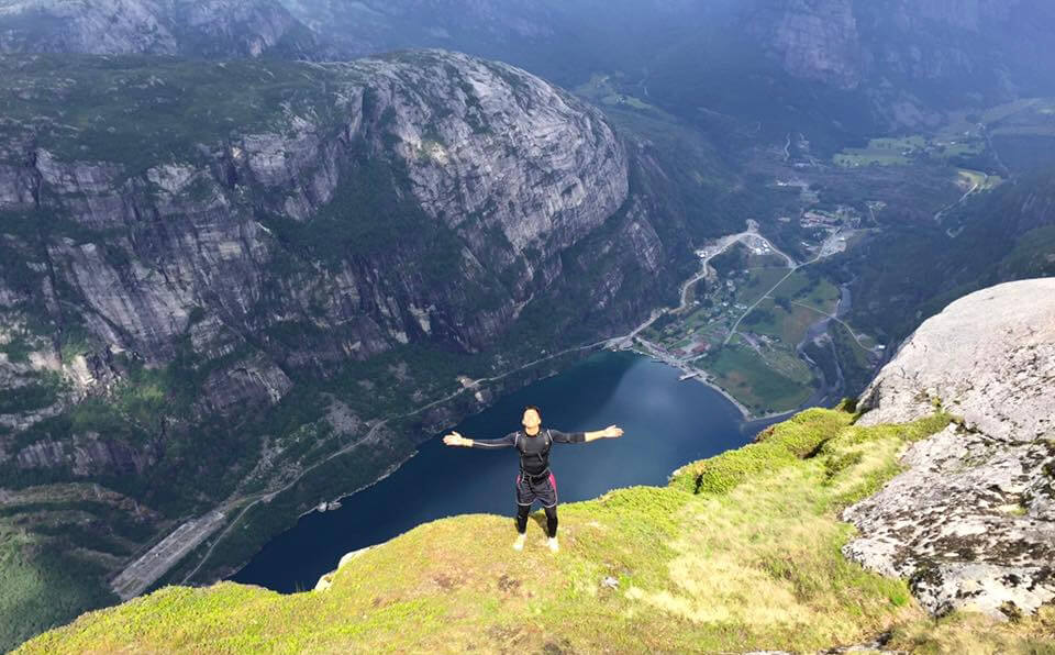 A man wearing black long sleeve, black short and black pants on the edge of Kjerag Mountain with the arms open and  the Lysefjord on the background