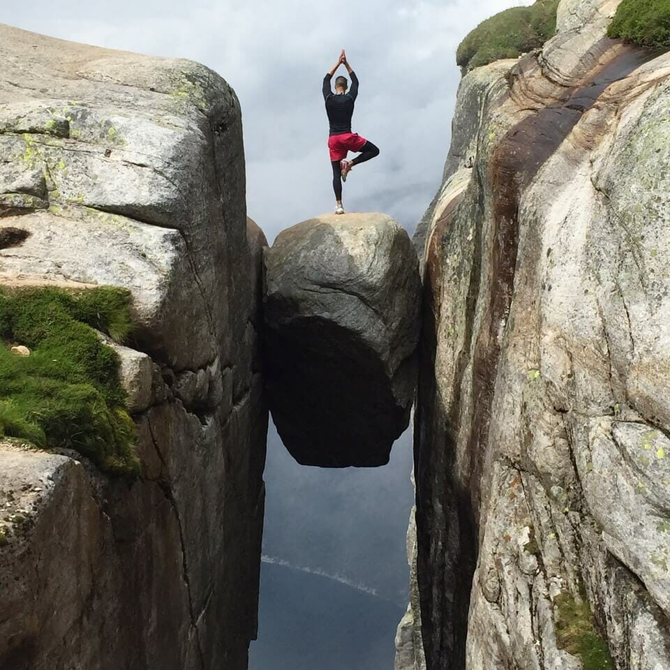 Pericles Rosa wearing a black long sleeve, black tights and red shorts doing a yoga tree pose on the top of Kjeragbolten