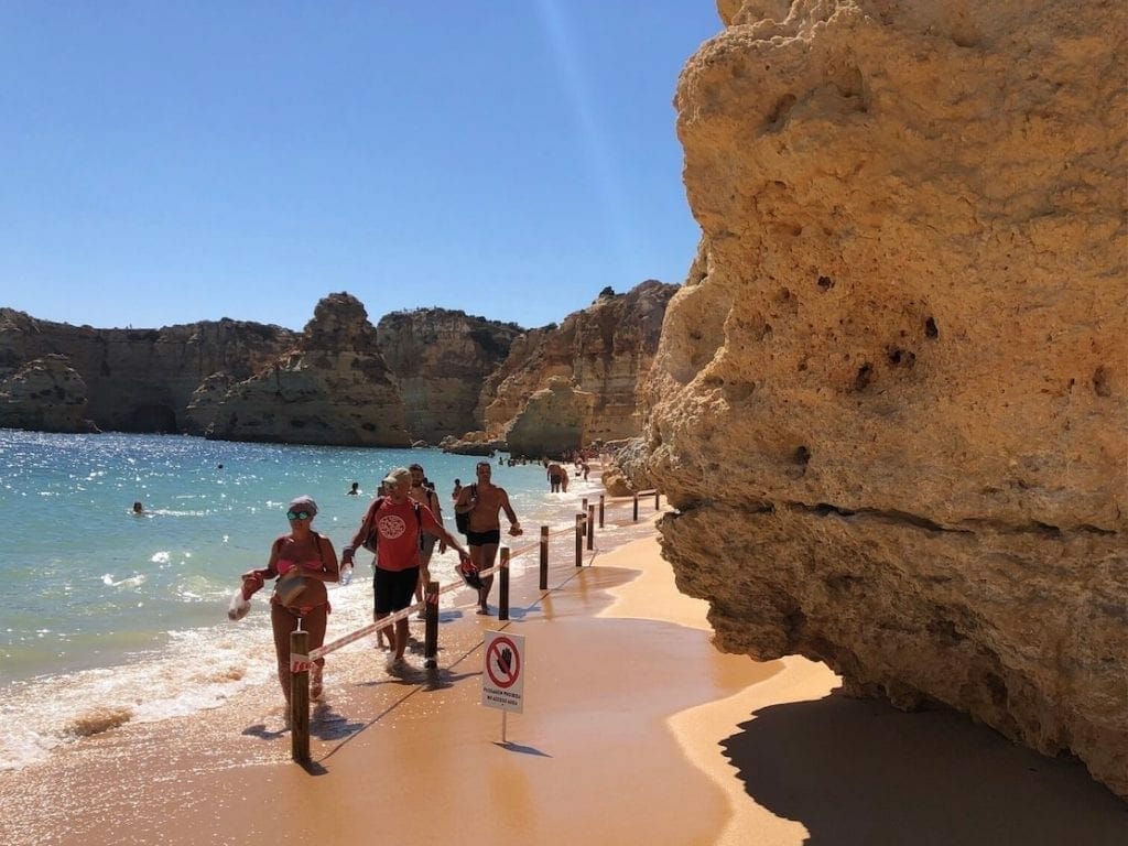 People walking on the beach near some massive yellow cliffs on Marinha Beach at high tide