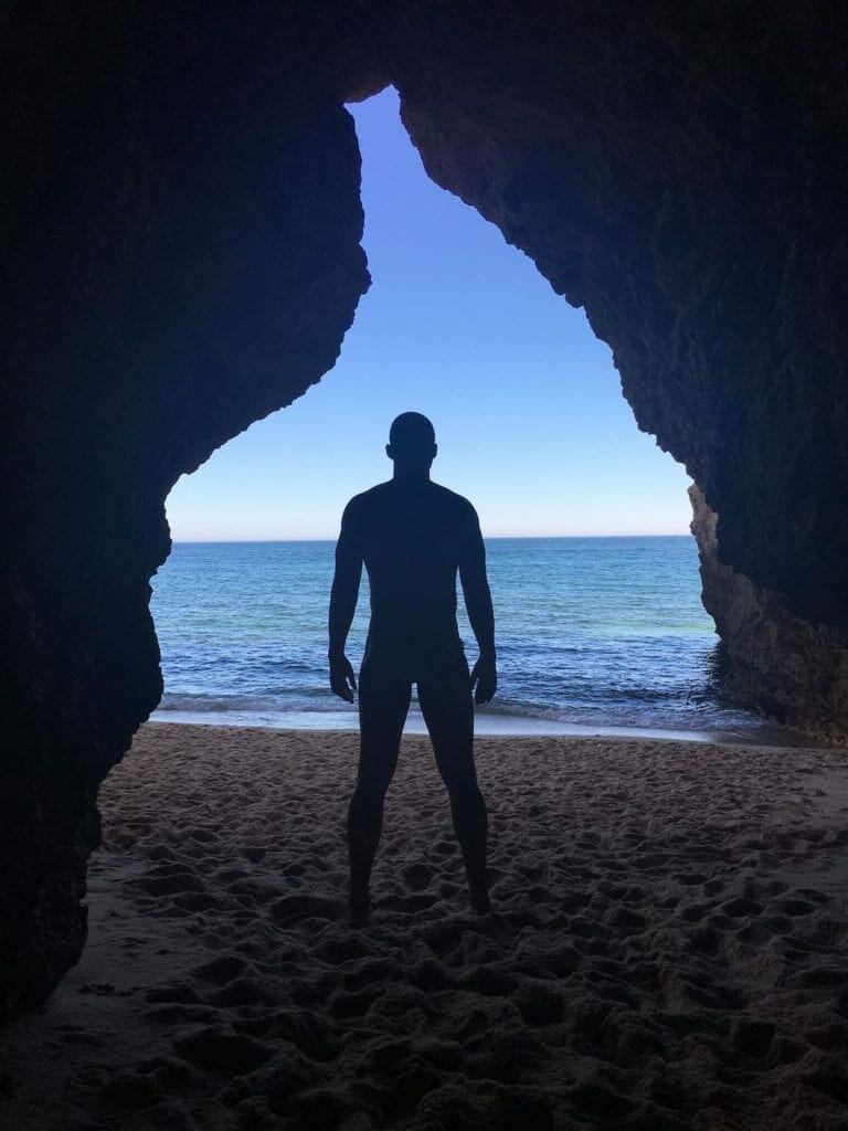 A man standing in front of the Praia da Buraco in the Algarve, Portugal, underneath a whole on the cliff