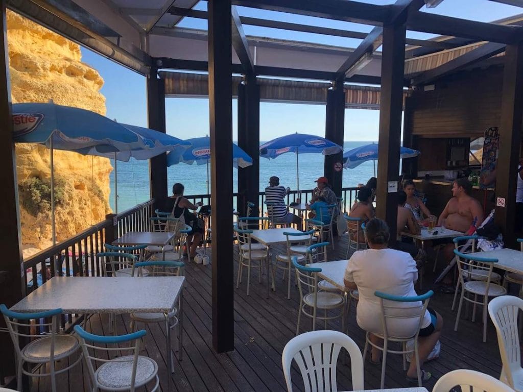 Praia da Marinha beachfront restaurant with some tables, chairs, umbrellas and people enjoying the view and talking