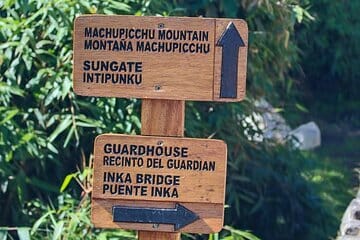 Two wooden signs: one for Machu Picchu Moutain and Sungate and the other written on black Guardhouse and Inka Bridge.