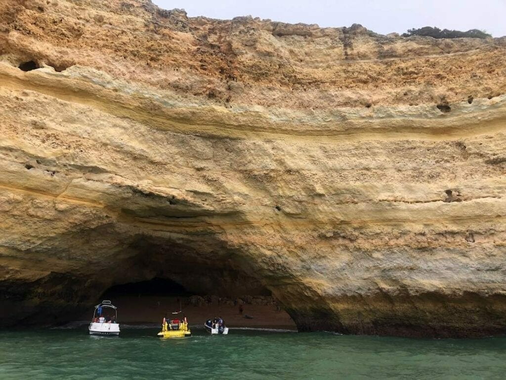 Two white boats and an yellow one entering a sea cave in the village of Benagil, Portugal