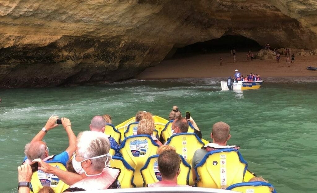 people on a boat wearing yellow lifejackets sailing in front a sea cave during a dolphin watching tour in the Algarve Coast, Portugal