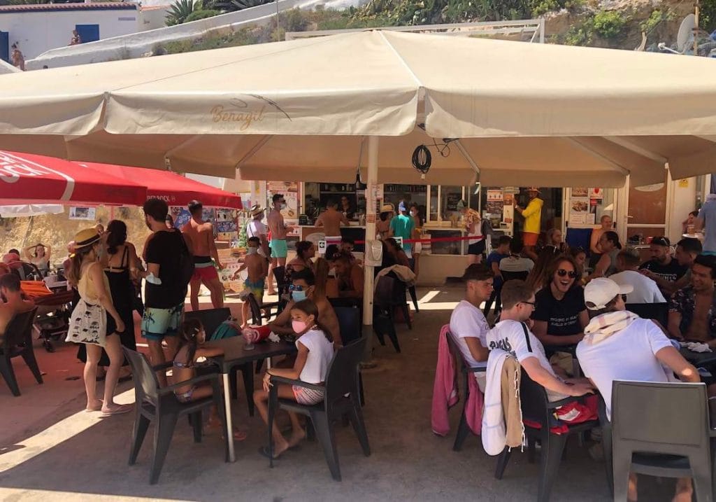 People sitting on chairs and some tables underneath a big white umbrella on a restaurant at Praia de Benagil